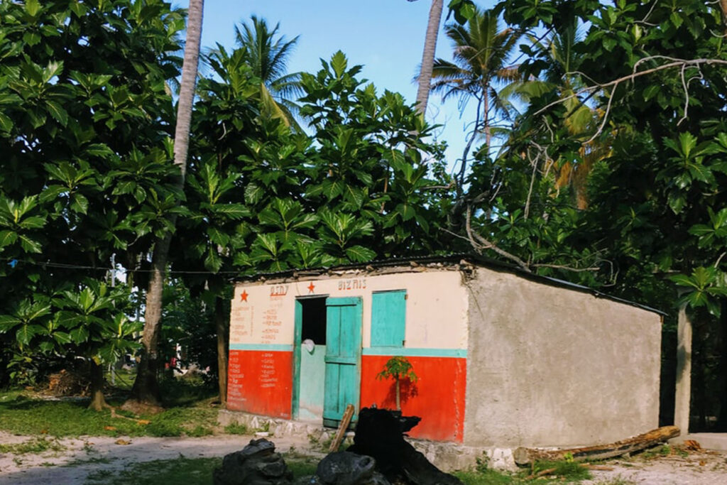 a building in Haiti with a green door and painted red surrounded by greenery | Claudia Altamimi – Unsplash