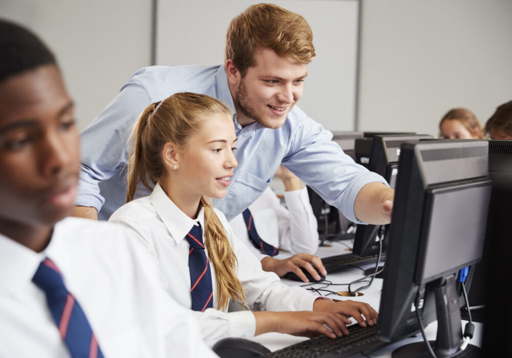 Male teacher helping teenage students on computers